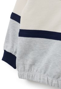 Mangas de sudadera en gris claro y crema con puños y bandas de canalé en azul marino, dobladillo de elástico recogido, en textura de tela suave.