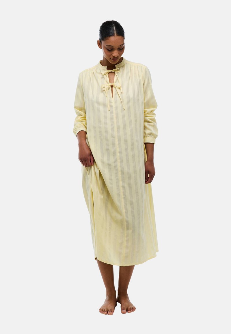 Robe midi jaune à rayures avec un col rond, des manches longues et un système de fermeture à cordon au col. Tissu doux et léger avec une coupe ample.