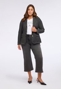 Šedý džínový blejzr s klopami, v kombinaci s bílým tričkem s potiskem a šedými zkrácenými džíny. Černé slingback podpatky doplňují celý outfit.