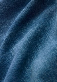 Denimstof in donkerblauw, met een gestructureerde uitstraling en een zachte afwerking. De stof vertoont subtiele variaties in kleur en weefpatroon.