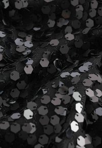Tissu en maille noire orné de paillettes hexagonales noires, réfléchissant la lumière et créant un aspect texturé et superposé.
