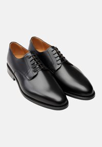 Chaussures de ville en cuir noir avec une finition lisse, bout pointu et piqûres décoratives. Comprend un laçage et un talon en bois.