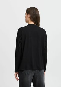 Top nero a maniche lunghe realizzato in tessuto testurizzato a coste. Presenta un collo tondo e una vestibilità comoda, abbinato a jeans scuri.