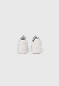 White sneakers featuring a textured design with repeating logo pattern, padded collar, and smooth texture on the body and sole.