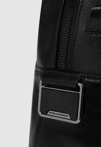 Zwarte leren rugzak met een gestructureerde afwerking, met een metalen ritssluiting en een rechthoekige zilveren hardware-accent met logo.