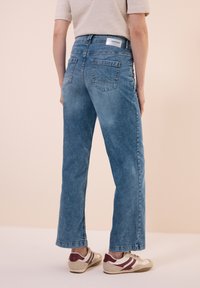 Jeans en denim bleu clair avec une coupe droite, taille haute et deux poches à l'arrière. Fini avec une petite étiquette portant la mention "BONHEUR". Portés avec des baskets décontractées.