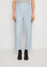 Helle blaue plissierte Hosen aus weichem Stoff, mit einem hochgeschnittenen Design und weitem Bein, kombiniert mit schwarzen Stiefeletten.