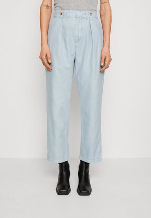 Pantalons plissés bleu clair en tissu doux, avec une taille haute et des jambes larges, associés à des bottines noires.