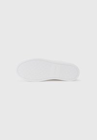 Talpa de sneaker albă cu un grip din cauciuc texturat, având un model geometric și un detaliu logo mic în apropierea călcâiului.