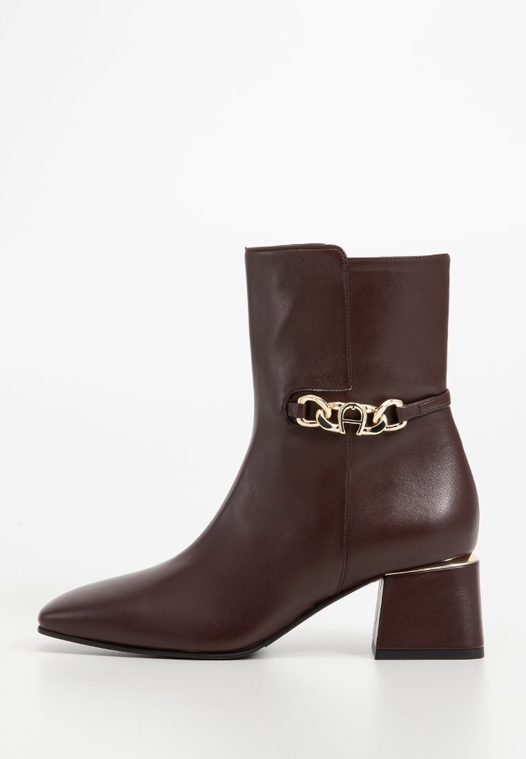 Brązowe skórzane botki za kostkę z ostrym noskiem, złotym łańcuchem na kostce oraz kwadratowym obcasem. Gładka faktura i elegancki design.