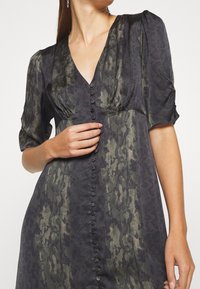 Black and green patterned dress with a V-neck, short puff sleeves, and a button-down front. The fabric has a smooth, slightly textured finish.