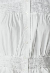 Weißes Kleid mit durchgehenden Knöpfen, mit gerafftem Oberteil und Taillenband. Glatter Stoff, geraffte Textur und sanfte Silhouette.