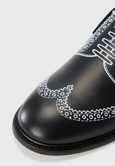 Black leather shoe with white decorative stitching featuring a detailed pattern along the edges and a rounded toe. Classic lace-up design.
