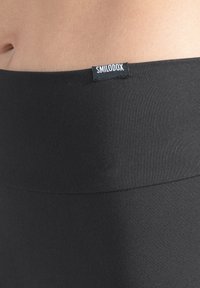 Svarta högmidjade leggings i mjukt, stretchigt tyg. Inkluderar en liten etikett med varumärket "SMILOOOX" på midjebandet.