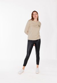 Camicia beige a maniche lunghe con un accento a stampa leopardata, abbinata a pantaloni attillati neri in ecopelle e sneakers bianche.