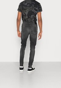 Úzké, tmavě šedé džíny s texturovanou tkaninou, elastickým pasem a zadními kapsami. V kombinaci s černým maskáčovým tričkem a černými teniskami.