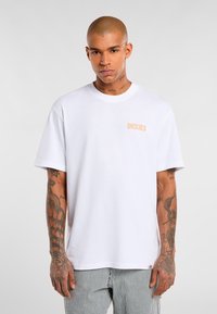 Bílý bavlněný tričko s kulatým výstřihem a krátkými rukávy, s oranžovým logem "DICKIES" na levé hrudi.