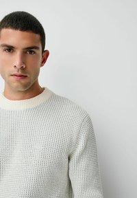 Pulover texturat de culoare gri deschis, cu un guler gros, de culoare albă-crem, cu striații. Designul prezintă un model tricotat în stil vafe și un decolteu rotund.