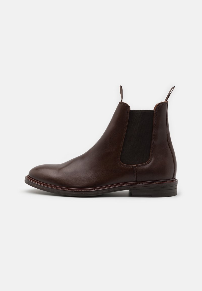 Botte Chelsea en cuir marron avec panneaux latéraux élastiques, bout rond et petit talon empilé. Dotée de languettes à la bordure pour un enfilage facile.