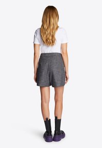 Pantalones cortos a cuadros en blanco y negro con un ajuste entallado, combinados con una camiseta blanca sencilla y botas de plataforma gruesas en negro y morado.