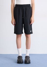 Čierne šortky po kolená vyrobené z ľahkej tkaniny, s elastickým pásom a malým bielym logom Nike na dolnej časti nohy.