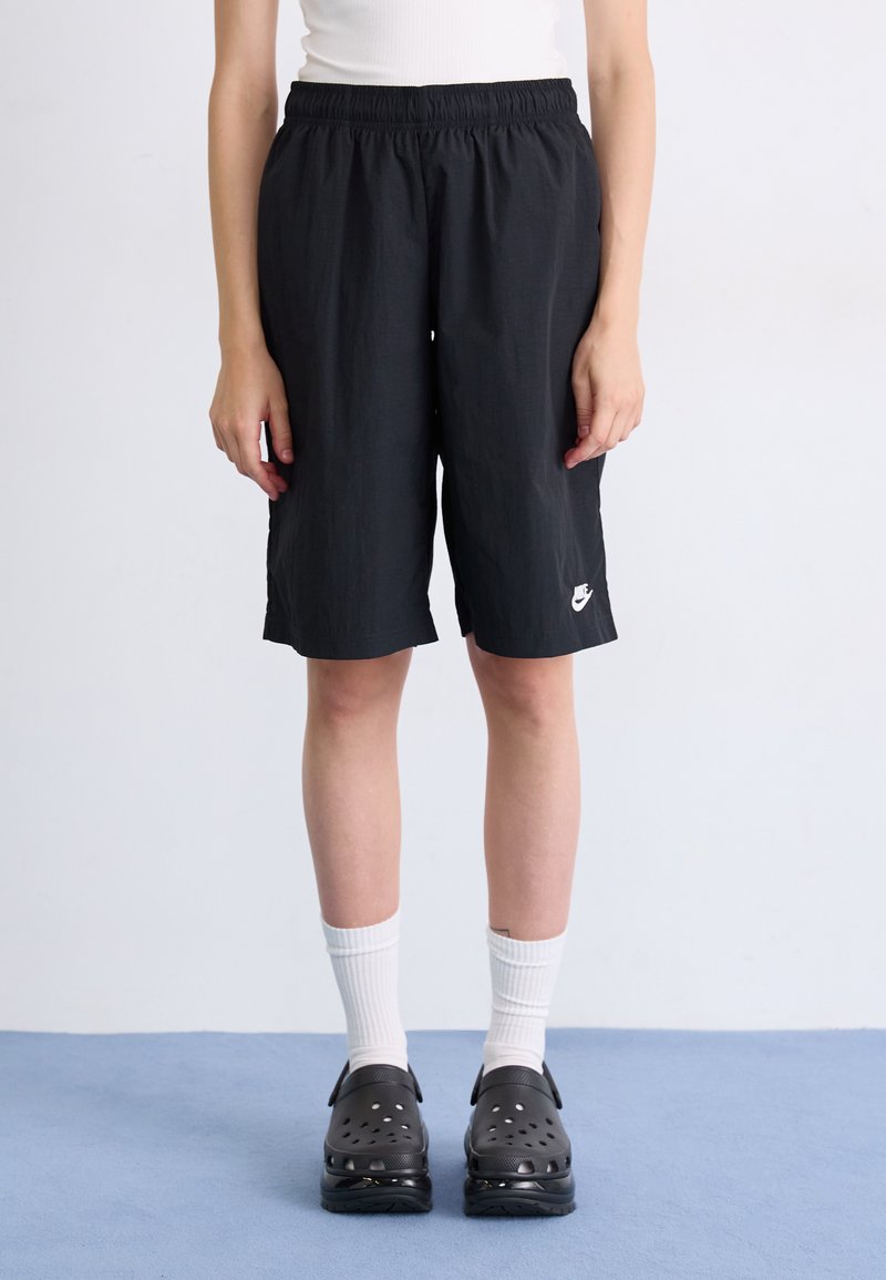 Čierne šortky po kolená vyrobené z ľahkej tkaniny, s elastickým pásom a malým bielym logom Nike na dolnej časti nohy.