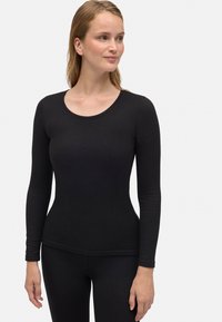 Top negro de manga larga en tejido elástico con escote redondeado. Diseño ajustado con textura suave, combinado con leggings negros.