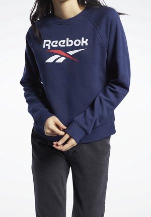 Felpa blu navy realizzata in misto cotone, con logo "Reebok" bianco e dettagli rossi, polsini e orlo a coste, e vestibilità rilassata.