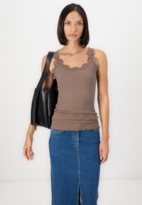 Débardeur marron côtelé avec dentelle, associé à une jupe en denim bleue avec une fente sur le devant. Le modèle porte un sac fourre-tout en cuir noir.