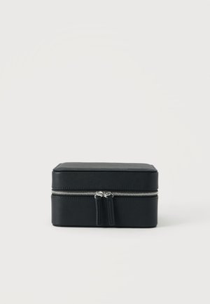 Étui de voyage rectangulaire en cuir noir avec fermeture éclair argentée et deux curseurs, posé sur un fond blanc uni.