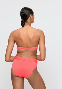 Korallinvärinen ribbineppariolkaimilla ja kiinnityksellä takana. Korkeavyötäröisissä alaosissa on leveä vyö, sileä pinta ja saumaton muotoilu.