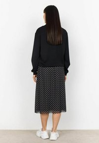 Felpa nera con maniche lunghe, abbinata a una gonna nera a pois. Presenta una texture fluida e pois bianchi. Indossata con sneaker bianche.