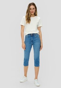 Jeans capri en denim bleu clair avec une taille haute, fermeture à deux boutons et une coupe slim. Associés à un t-shirt blanc uni et des baskets blanches.