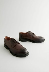 Chaussures en cuir marron à lacets avec une surface texturée et une semelle en caoutchouc noire contrastante ; elles présentent un bout arrondi et des détails de couture subtils.
