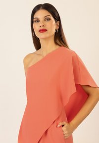 Vestido de coral asimétrico con un hombro, tejido suave, corte holgado y bolsillo lateral. Textura suave y detalles de diseño fluidos.