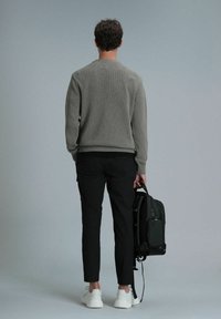 Grijze gebreide trui met een ronde hals, zwarte slim-fit broek en witte sneakers, met een donkergroene stoffen rugzak.