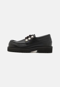 Mocasines de cuero negro con punta redonda, que presentan tres acentos metálicos y una suela texturizada para mayor agarre. Parte superior lisa y detalle de costura.