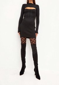 Vestido mini negro acanalado con un corte, mangas largas y costuras verticales. Combinado con medias a rayas negras y botas negras hasta la rodilla.