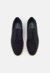 Chaussures en daim bleu marine foncé avec une texture lisse, bout rond et deux paires de lacets assortis. Semelle en caoutchouc marron avec des détails cousus.