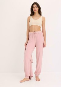 Pantaloni in pigiama rosa chiaro con vestibilità morbida, vita con cordoncino e top a coste color crema. Tessuto morbido, design rilassato e costruzione semplice.