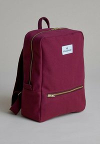 Mochila de tela burdeos con forma rectangular, un bolsillo frontal con cremallera y una etiqueta de logo blanca. Presenta correas de hombro ajustables.