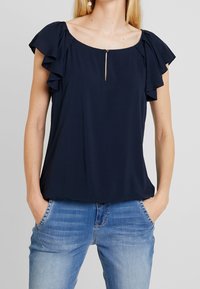 Marineblaue Bluse mit Rüschenschlaufen und einem Schlüssellochdetail vorne. Gefertigt aus leichtem Stoff, bietet sie einen lockeren Schnitt und einen runden Halsausschnitt.