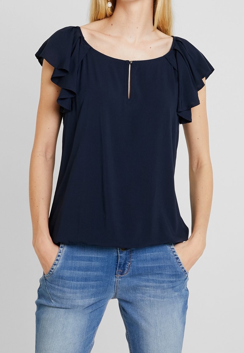 Marineblaue Bluse mit Rüschenschlaufen und einem Schlüssellochdetail vorne. Gefertigt aus leichtem Stoff, bietet sie einen lockeren Schnitt und einen runden Halsausschnitt.