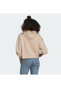 Ljusrosa croppad hoodie med dragsko i huvan, mjuk textur och vida ärmar, tillsammans med medelhöga blå denimjeans.