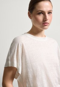 Helles Beige, kurzärmeliges T-Shirt aus strukturiertem Stoff. Rundhalsausschnitt mit umgeschlagenen Ärmelbündchen und lockerer Passform.