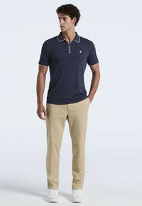 Polo shirt marine avec bord blanc, manches courtes et tissu texturé. Associé à un pantalon beige clair et des baskets blanches.