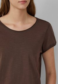 Brązowa bluzka z krótkim rękawem i okrągłym dekoltem. Tkanina ma teksturowany, lekko melanżowy wygląd. Prosty design z minimalnymi detalami szwów.