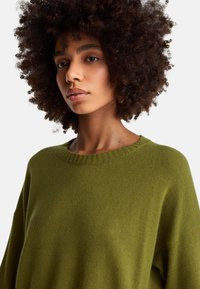 Olivově zelený pletený svetr s žebrovaným výstřihem a volnými rukávy, s jemnou texturou a minimalistickým designem.