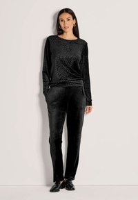 Zwart velours lange mouwen top met luipaardprint, gecombineerd met bijpassende zwarte velours broek. Beide hebben een gladde, zachte textuur en een relaxte pasvorm.