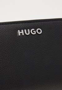 Portafoglio in pelle nera con finitura testurizzata, logo "HUGO" in rilievo in metallo argentato e design pulito e minimalista.